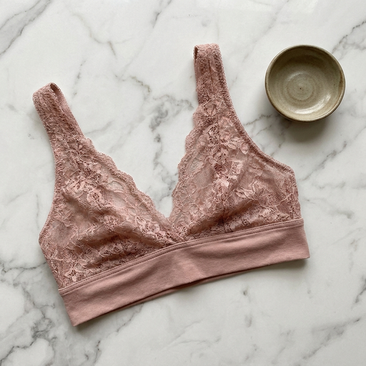 Bralette aus zartrosa Spitze mit breitem, weich eingefasstem Unterbrustbund auf hellem Marmor
