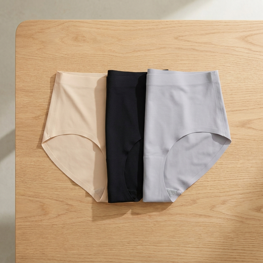 Drei nahtlose Slips mit hoher Taille in Beige, Schwarz und Hellgrau auf einer Eichenplatte